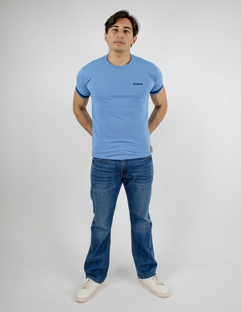 Hombre con camiseta azul claro, vaqueros y zapatillas blancas de pie sobre un fondo blanco liso.