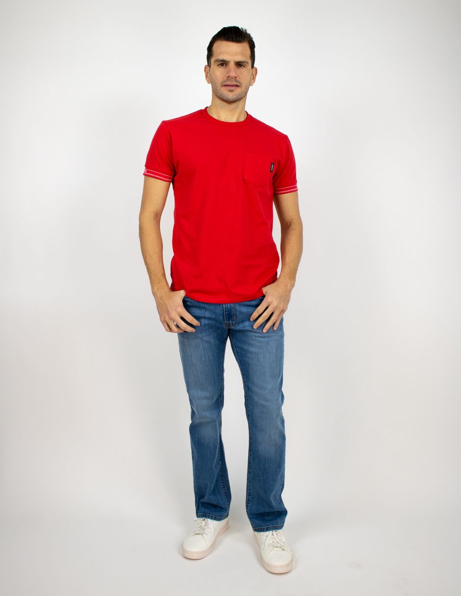 Hombre de pie sobre un fondo blanco, con camiseta roja, vaqueros azules y zapatillas blancas.