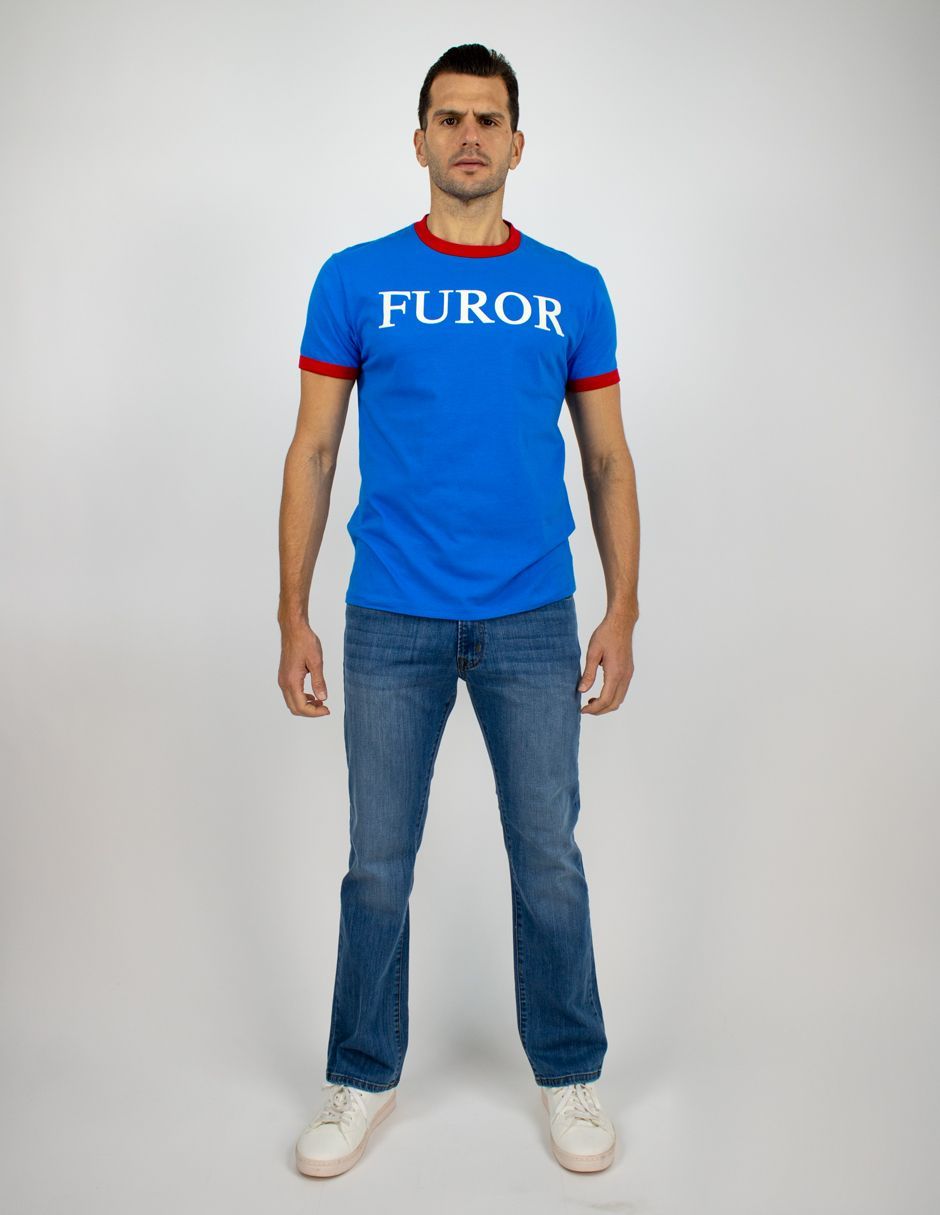 Hombre de pie frente a un fondo liso, vistiendo una camiseta azul con la palabra