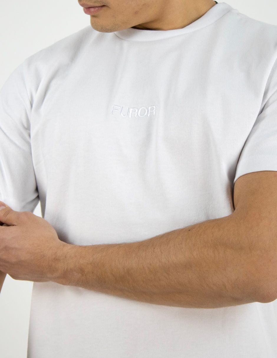 Persona con una camiseta blanca lisa y los brazos cruzados sobre un fondo claro.