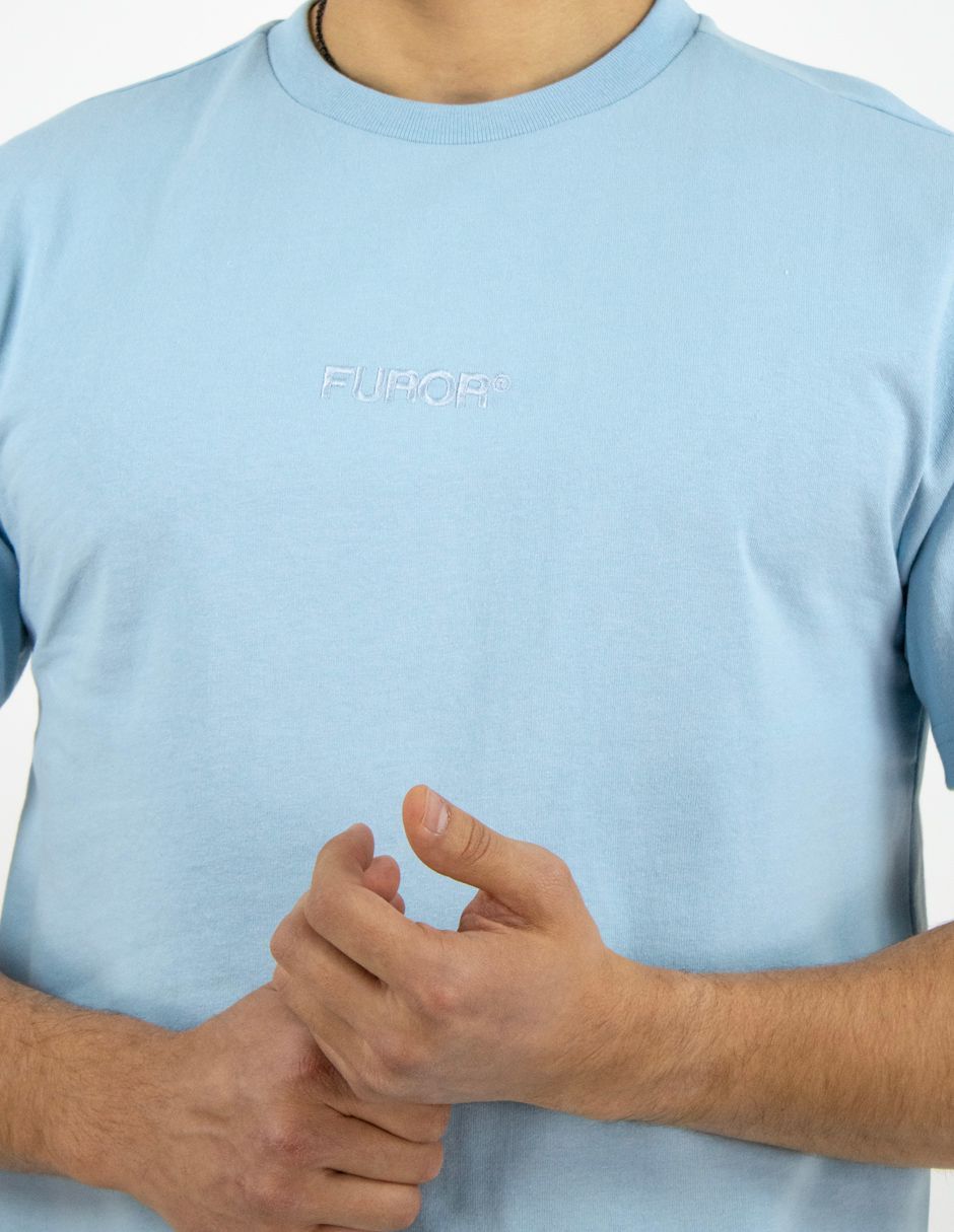 Persona con una camisa azul claro y las manos entrelazadas frente al pecho.