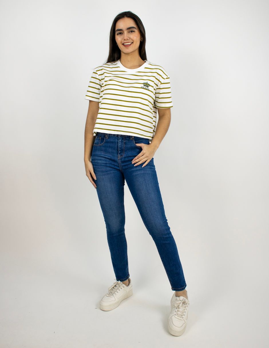 Mujer de pie sobre un fondo blanco, vestida con una camisa de rayas, vaqueros azules y zapatillas blancas.