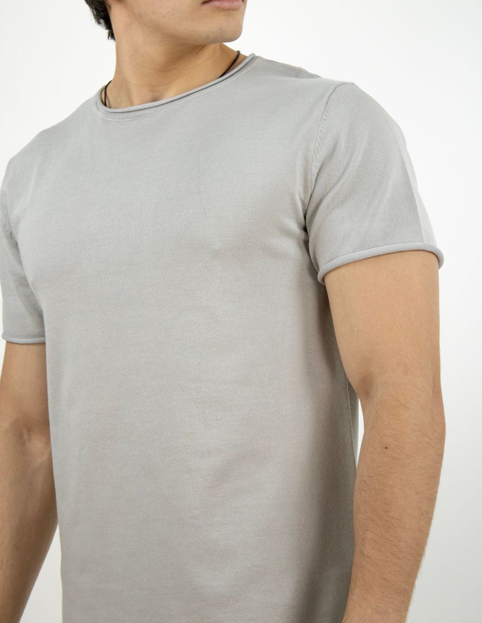 Persona con una camiseta gris claro de manga corta sobre un fondo blanco liso.