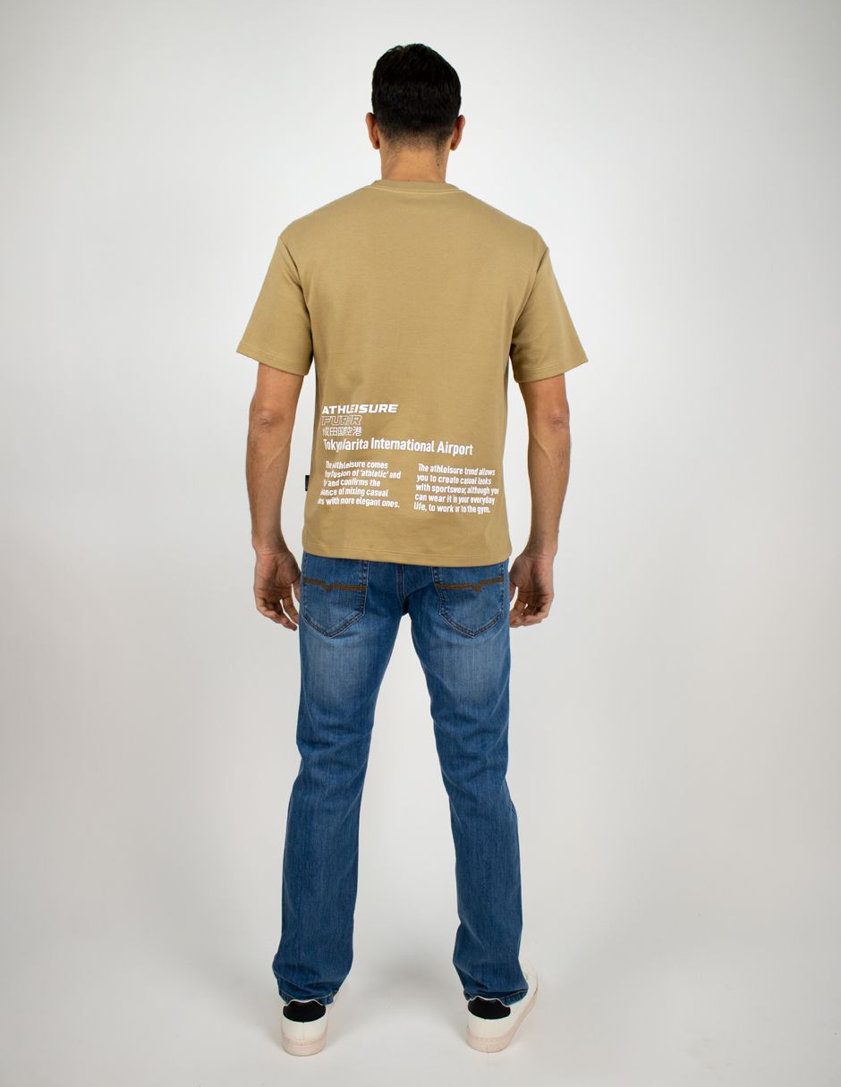 Hombre de pie de espaldas a la cámara, con una camiseta color canela y vaqueros azules sobre un fondo blanco.