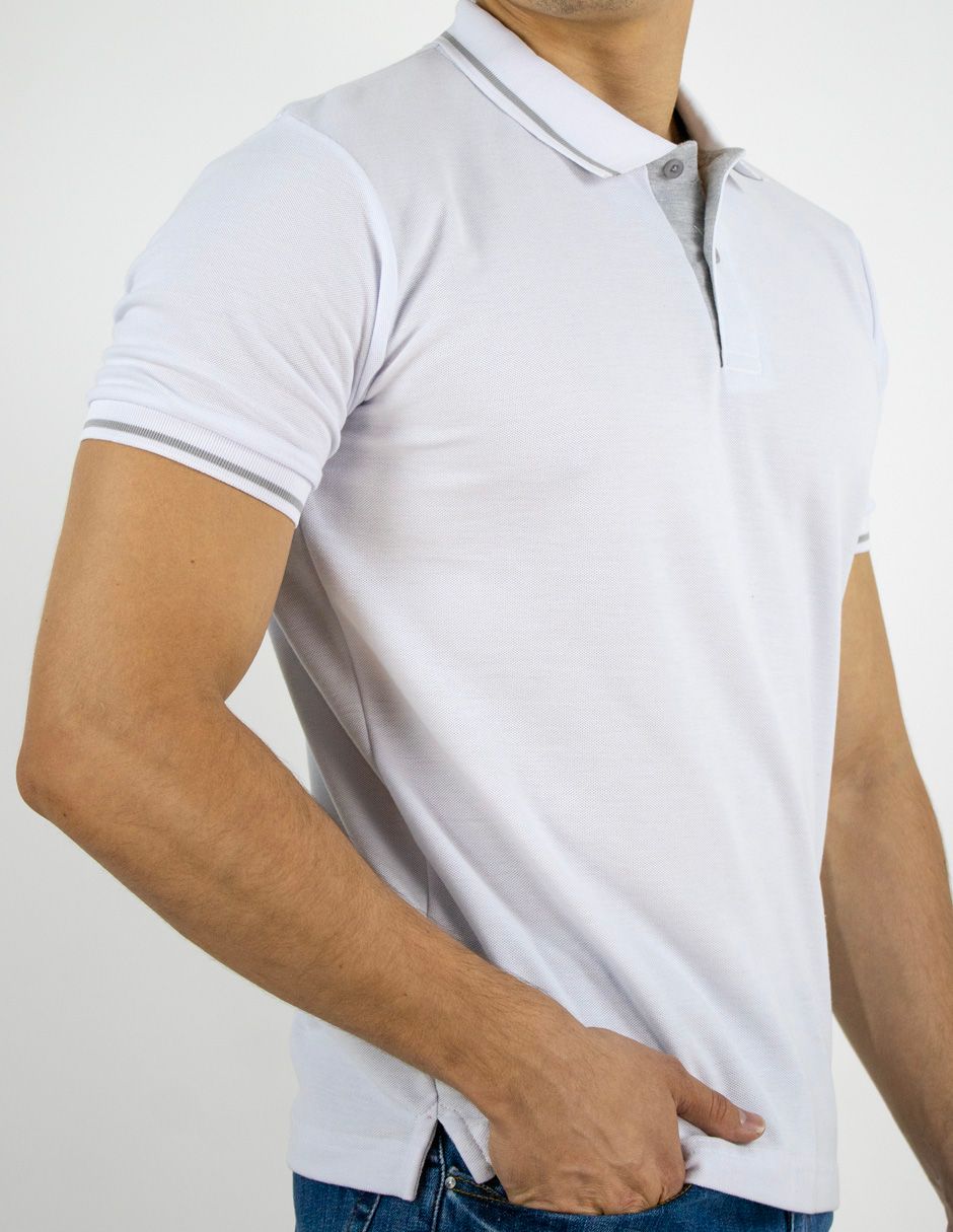 Hombre con polo blanco, visto desde el pecho hasta las caderas, con la mano en el bolsillo.