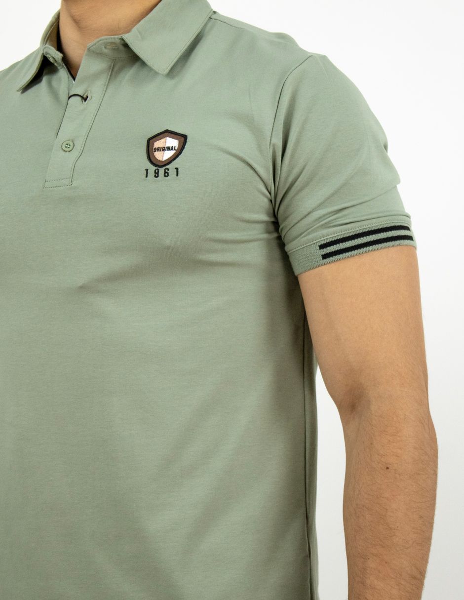 Primer plano de una camisa polo verde oliva con puños a rayas y un pequeño logotipo en el pecho.