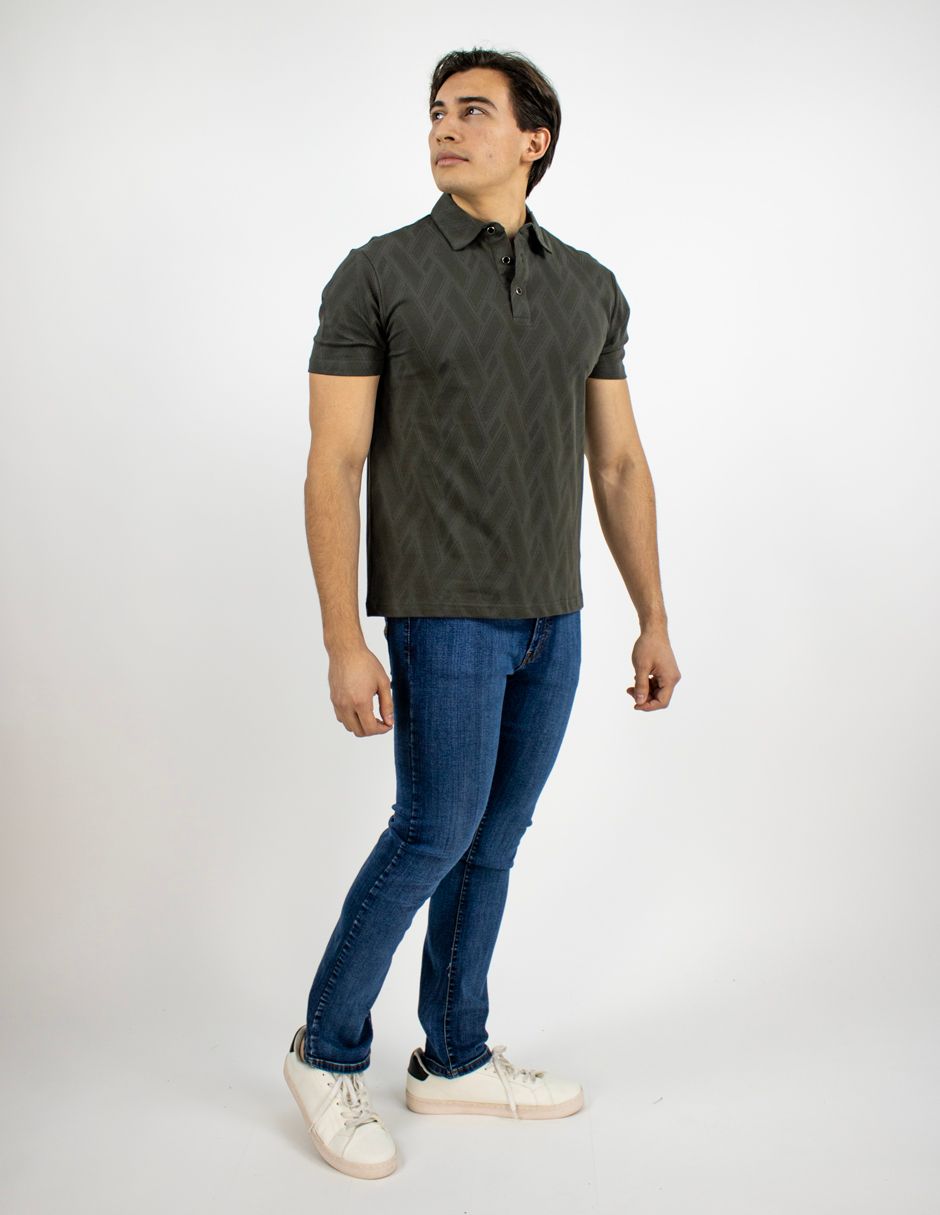 Hombre con polo oscuro, vaqueros azules y zapatillas blancas de pie sobre un fondo blanco.