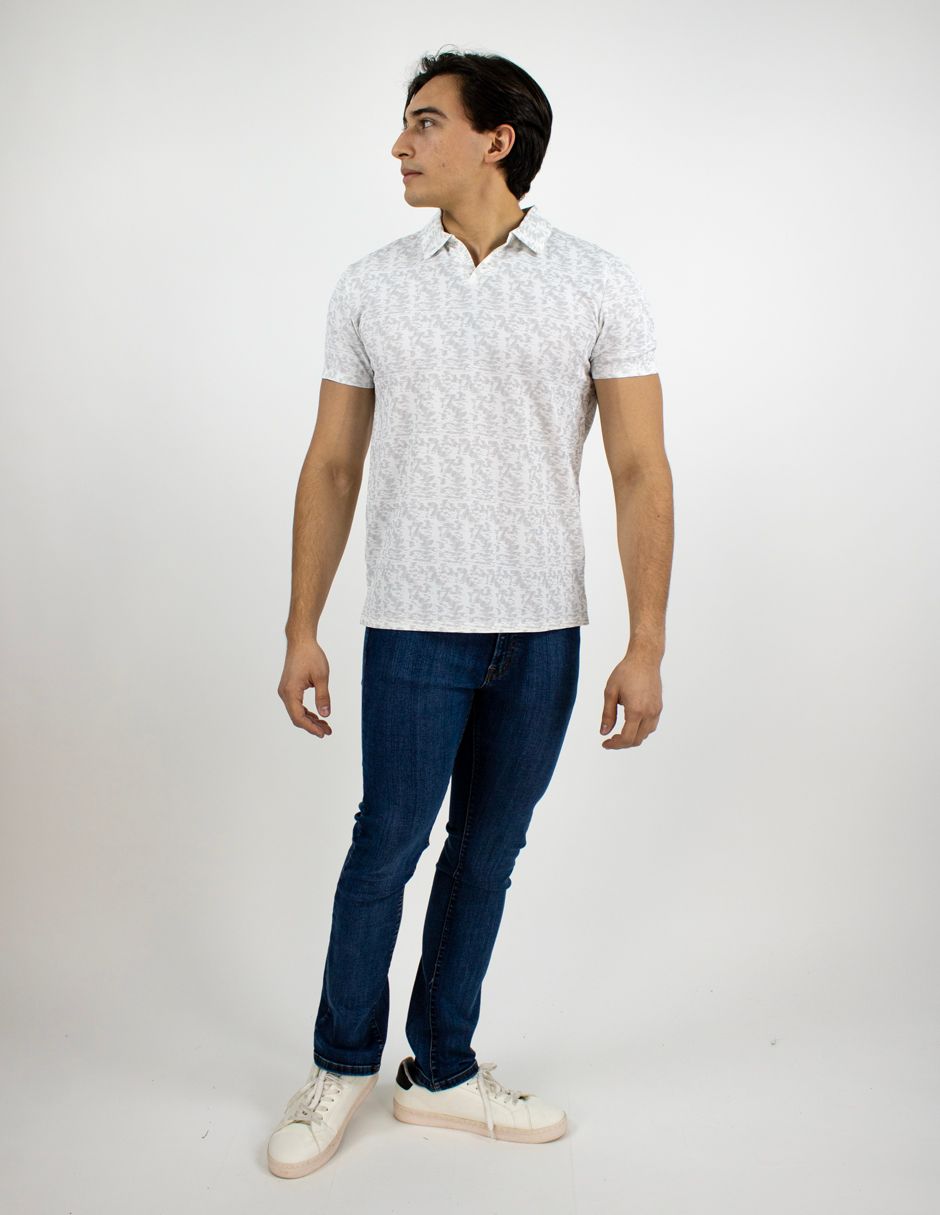 Persona de pie con una camisa polo blanca, vaqueros oscuros y zapatos blancos sobre un fondo blanco liso.