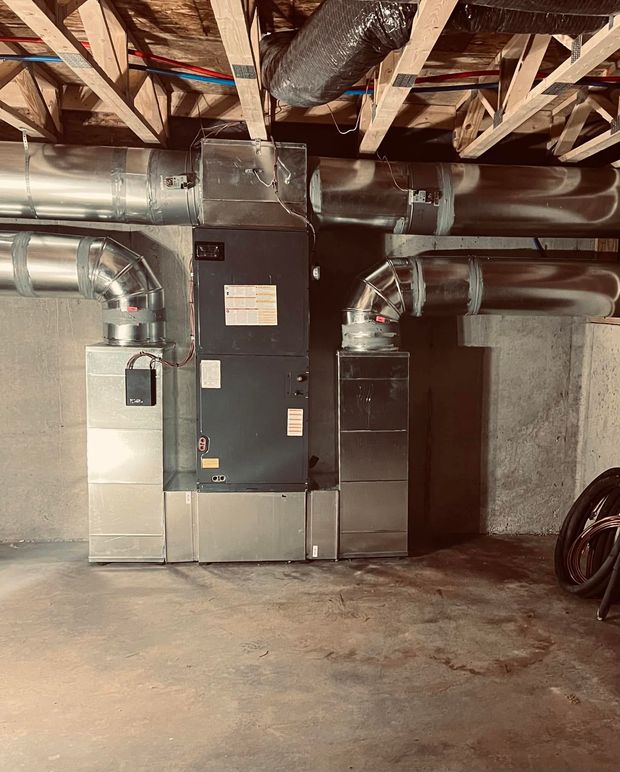 Basement utility room with large HVAC furnace units, exposed ceiling beams, and concrete floor