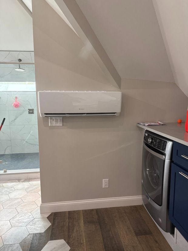 Small kitchen area with a wall-mounted mini split, blue cabinets, oven, and partial view of a tiled bathroom.
