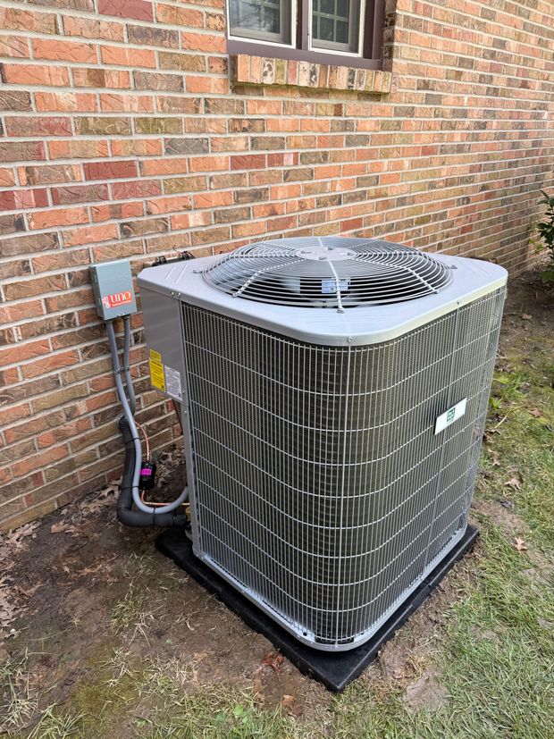 Outdoor HVAC condenser unit beside a brick house wall on a concrete pad.