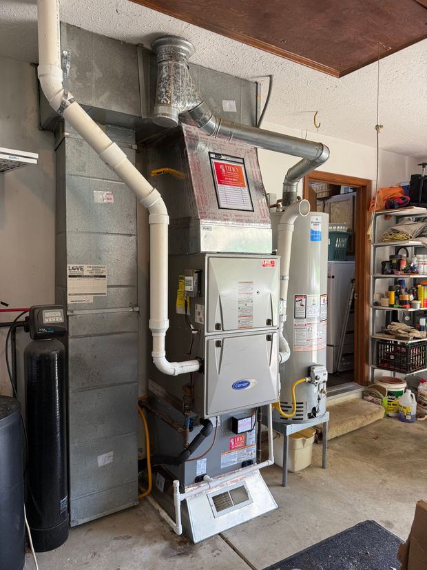 Furnace and HVAC units in a garage, with ductwork and storage shelves nearby.