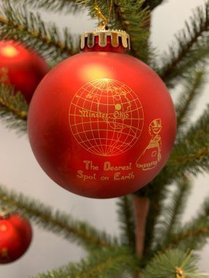 Red Christmas ornament with gold globe design hanging on a pine tree branch