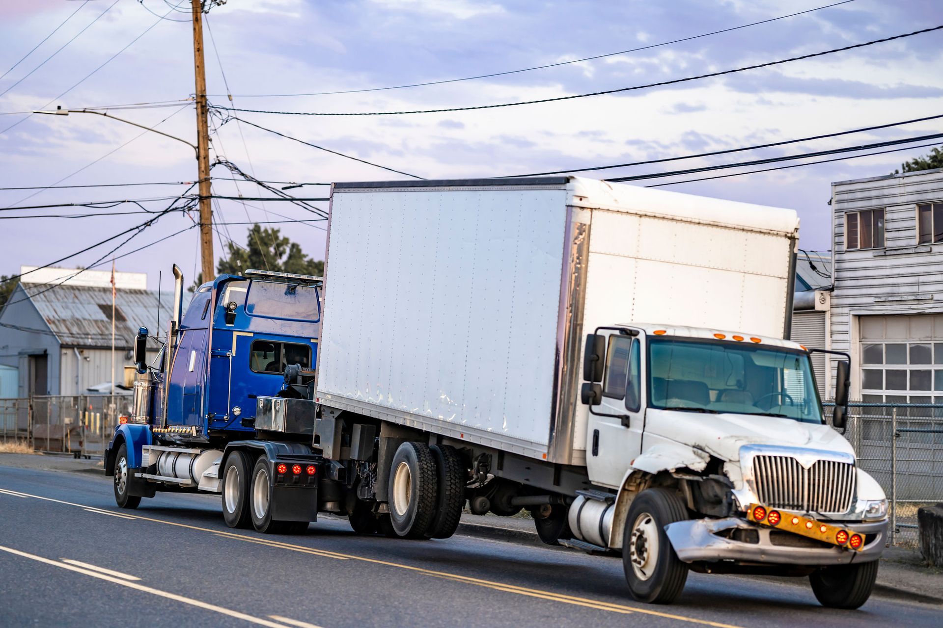 A semi-trailer truck towing a wrecked white truck in an urban area. A semi-trailer truck towing a wrecked white truck in an urban area.