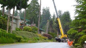 Yellow crane on a sloped residential street near homes and trees, with workers and orange cones nearby