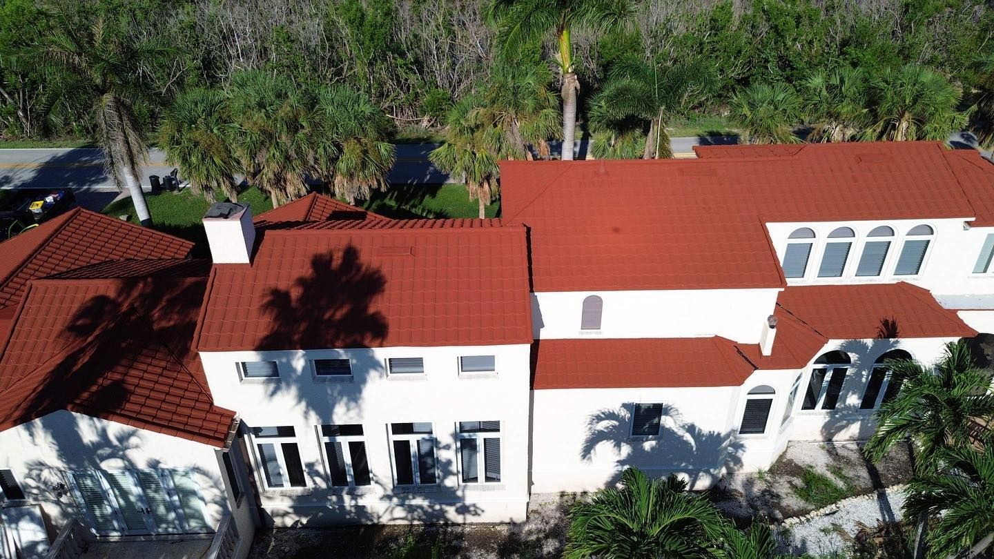 An aerial view of a large white house with a red tile roof surrounded by palm trees.
