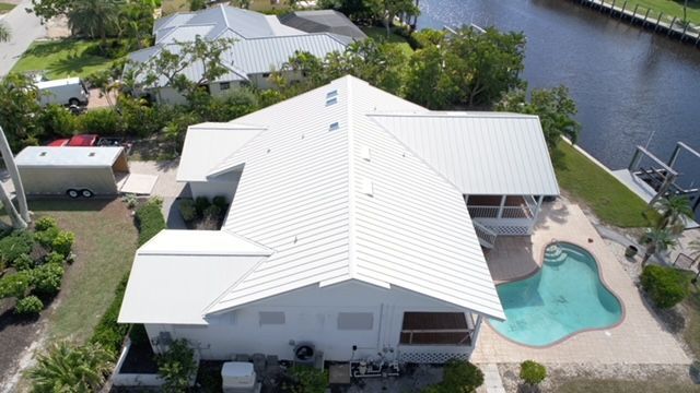 An aerial view of a house with a white roof and a pool.