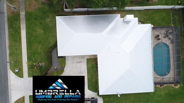 An aerial view of a house with a white roof and a pool.