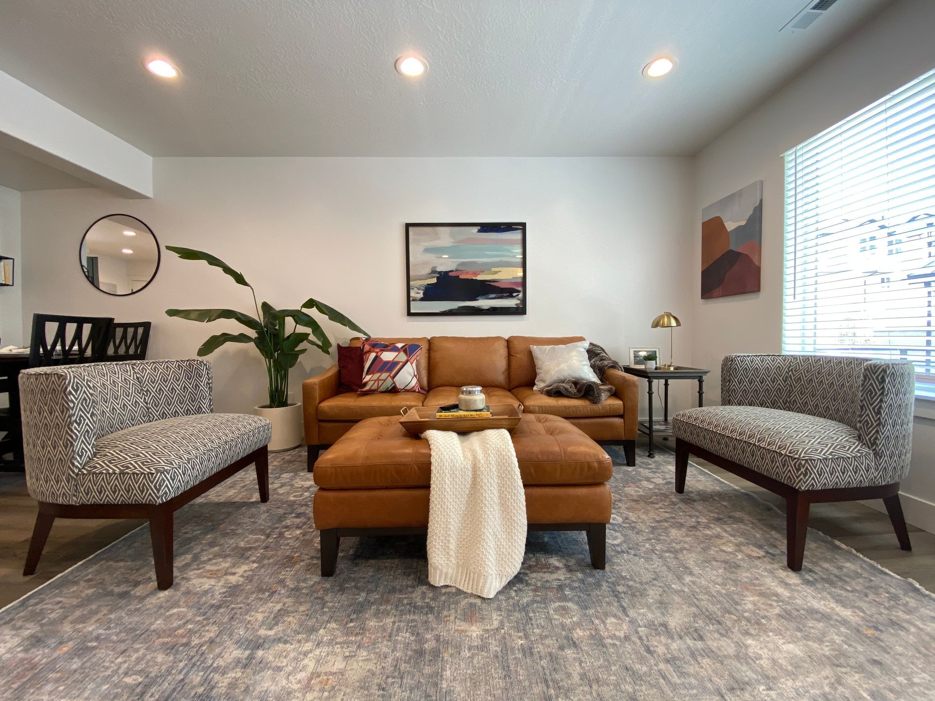 Cozy living room with tan sofa, patterned armchairs, gray rug, and wall art in bright natural light Madison Towns on 40th