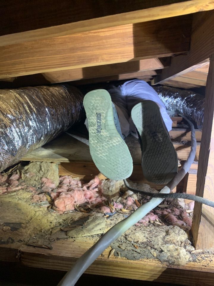 A person crawling through an attic space with insulated ductwork, wooden beams, and pink insulation visible.