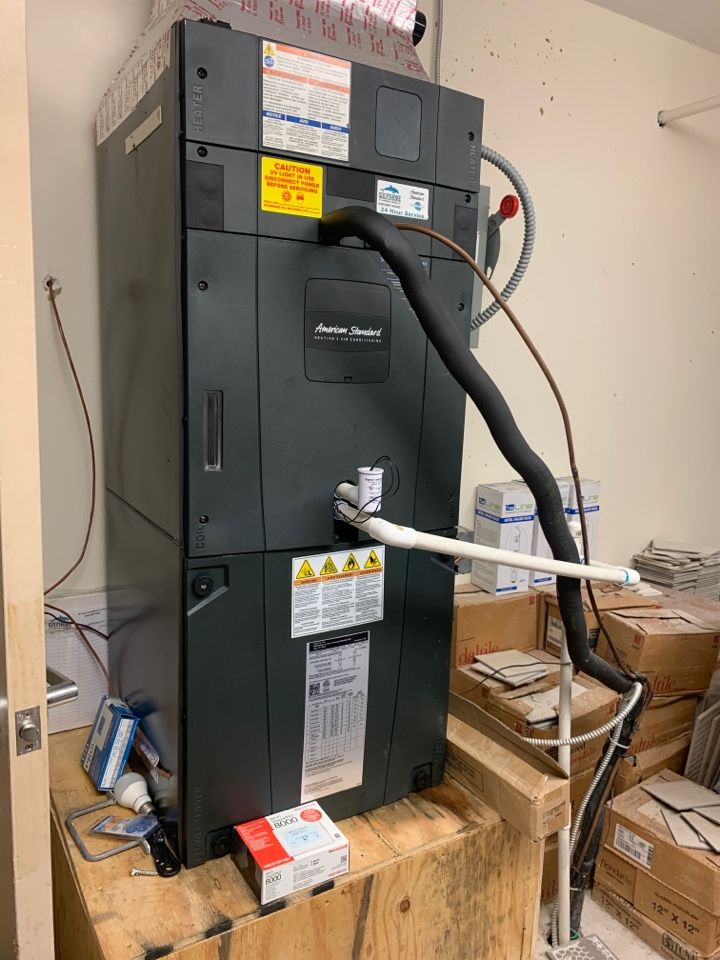 A black Carrier air handler unit sits on a wooden platform in a storage area, with attached pipes and electrical wiring.