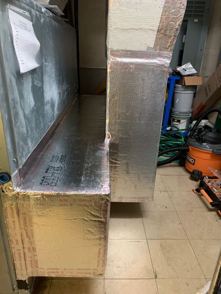 A metal duct system insulated with foil-faced board in a basement setting.