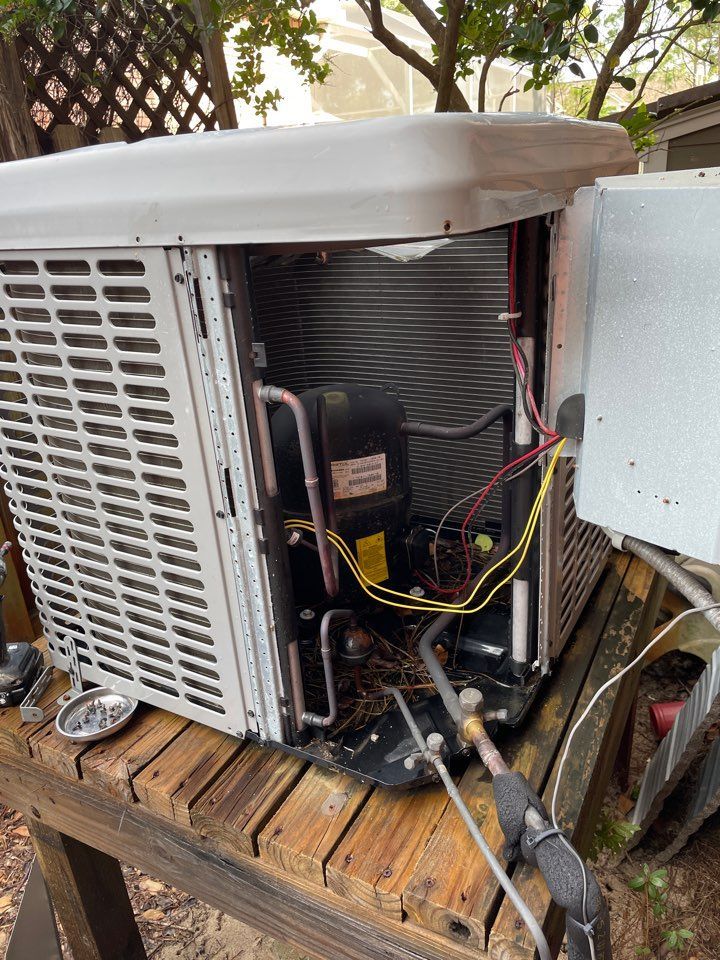 An outdoor air conditioning unit with its side panel removed, revealing internal mechanical components and wiring.