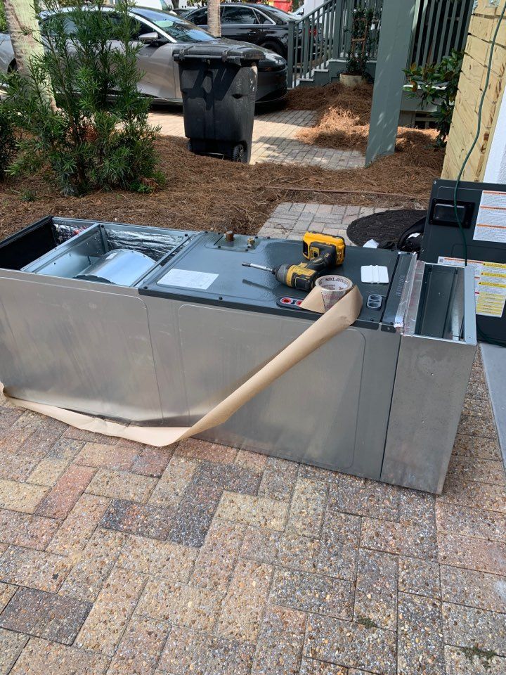 An HVAC air handler unit sitting on a brick driveway, with a power drill and tape on top during installation.