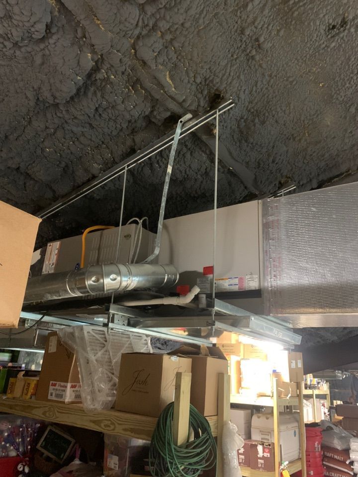 An HVAC unit suspended from the ceiling above metal storage shelves in a cluttered, dark room.