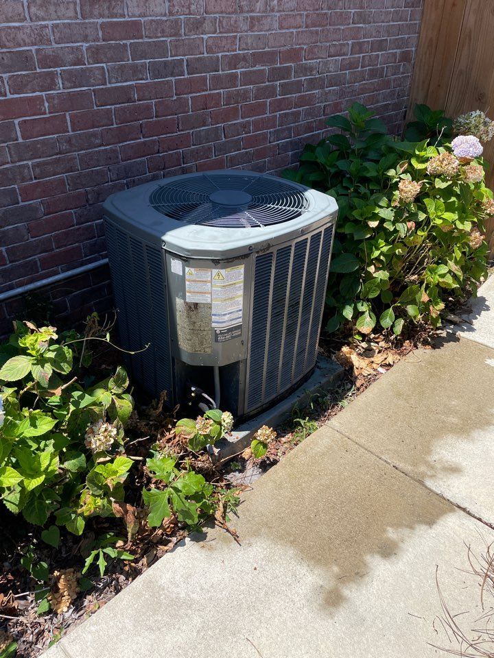Outdoor air conditioner unit beside a brick wall and garden bed with flowers
