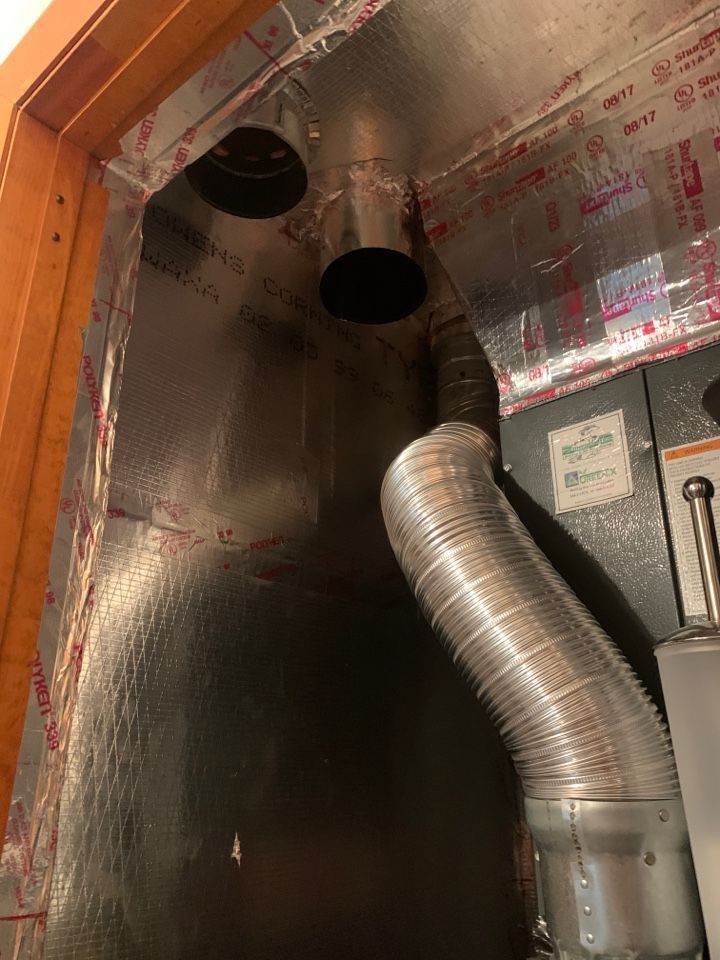Flexible metal ductwork connects to a rigid metal flue pipe extending from a furnace inside a closet.