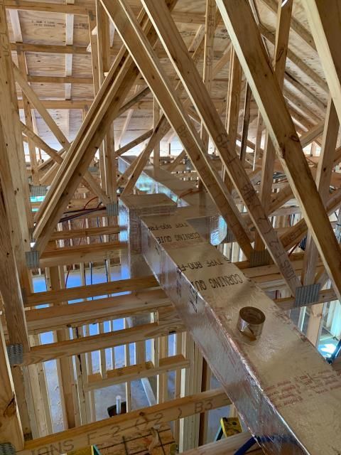 An interior view of exposed wooden roof trusses and an HVAC duct running through an unfinished residential construction site.