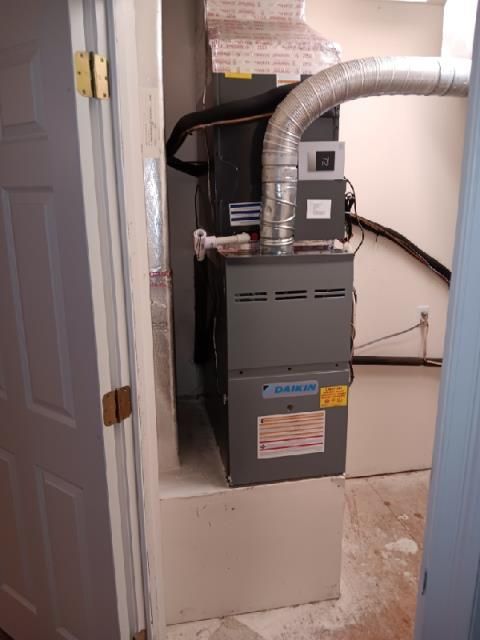 A grey Daikin HVAC unit installed in a utility closet, viewed from a doorway.