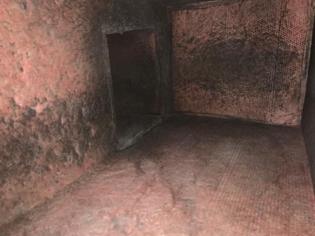 A dim, enclosed space with rough, textured, reddish-brown walls and a rectangular doorway leading to darkness.