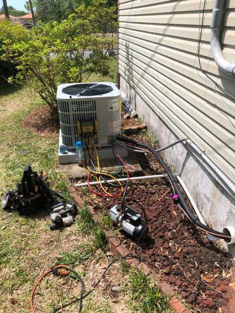 An HVAC technician's tools and a vacuum pump connected to an outdoor residential air conditioning unit.