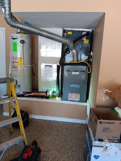 A water heater and a furnace unit installed in a recessed alcove in a room, with a ladder in the foreground.