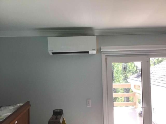A white wall-mounted air conditioner unit positioned near a glass door leading to an outdoor deck.