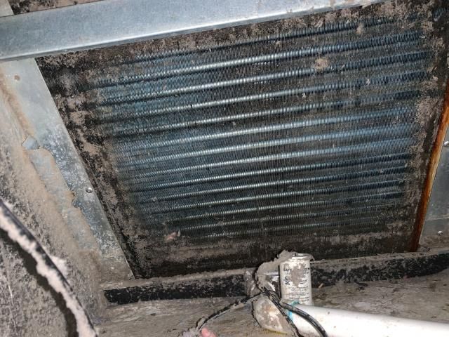 A dirty HVAC evaporator coil inside a metal housing, showing heavy accumulation of dust and debris on the cooling fins.