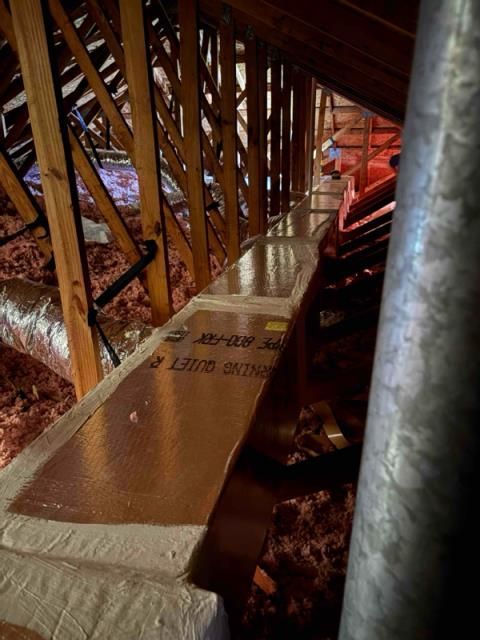 An attic interior showing wooden roof trusses, pink insulation, and a pathway lined with metallic-faced insulation boards.