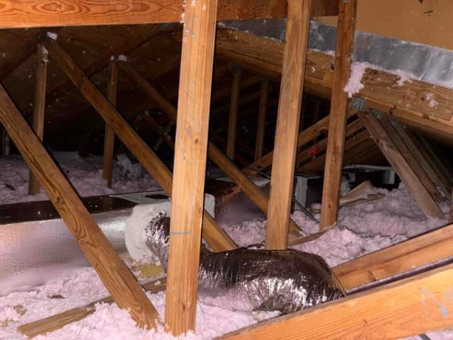 A view of an attic showing pink insulation, wooden roof rafters, and exposed metal air conditioning ducts.