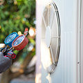 Two grey outdoor air conditioning units side-by-side against a horizontal siding wall.