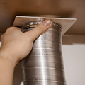 A dusty white wall air vent with a visible buildup of lint and debris, positioned near a floor and baseboard.