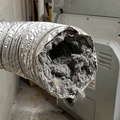 A dusty white wall air vent with a visible buildup of lint and debris, positioned near a floor and baseboard.