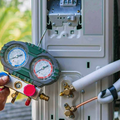 A technician in an orange uniform uses a manifold gauge set to service an outdoor air conditioning unit.