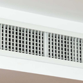 A white rectangular HVAC ceiling vent with a grid pattern mounted on a plain white surface.
