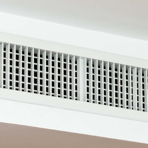 A white rectangular HVAC ceiling vent with a grid pattern mounted on a plain white surface.