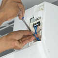 Hands using a screwdriver to connect blue wires inside a white wall-mounted air conditioner unit.