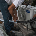 Hands using a screwdriver to connect blue wires inside a white wall-mounted air conditioner unit.