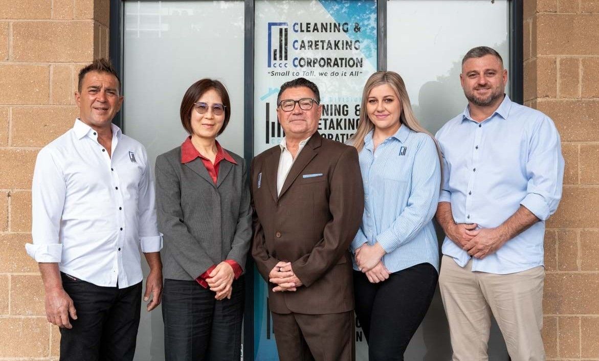 Five people standing outside a building entrance with a business sign behind them