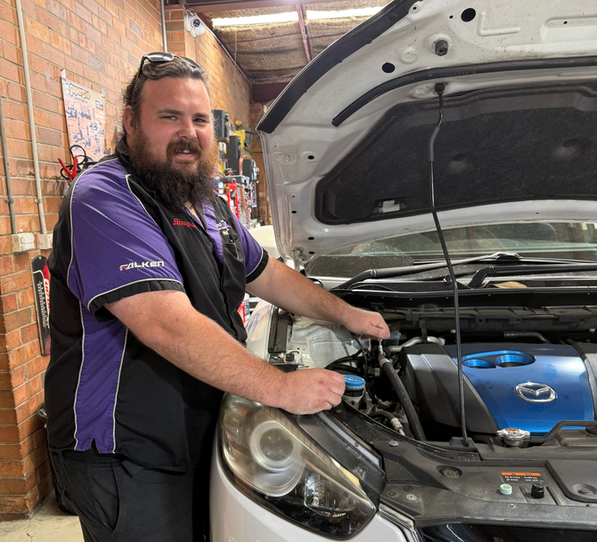 Mechanic smiling beside a car with the hood open in a garage — AutoHop Lambton in Lambton, NSW